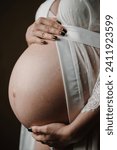 Small photo of Pregnant woman. Pregnancy motherhood procreation concept. Closeup belly of a woman. Female waiting for newborn baby. Young pregnant girl touching and holding her belly and caring about health indoors.