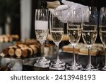 Catering service concept. The waiter pouring white sparkling wine. Barmen pours champagne into flute glasses. Champaign is being poured into glasses. Bottle in a closeup view. Rows of full glasses.
