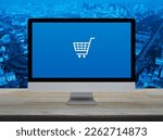 Shopping cart flat icon on desktop modern computer monitor screen on wooden table over city tower, street, expressway and skyscraper, Business shop online concept