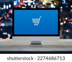 Shopping cart flat icon on desktop modern computer monitor screen on wooden table over blur colorful night light traffic jam road in city, Business shop online concept