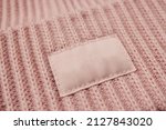 Small photo of Close-up of a light, pink woolen knitted hat, for a girl. Mock-up, a light-colored empty fabric tag sewn to a headdress for a logo or brand. A uniform. Teen brand, women's accessory