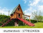 Small wood log playhouse hut with stairs ladder and wooden slide on children playground at park or house yard. Green grass lawn garden and blue clear sky in background on bright sunny summer day