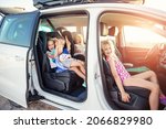 Group of four cute adorable little happy caucasian children enjoy having fun sit in minivan going to sea beach road trip on hot summer day. Kids in swimsuit in car with side open door against sun