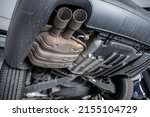 Small photo of Close-up detail bottom view of car part metal exhaust muffler pipe with rusty stains. Lifted vehicle check-up maintenace service, repair and fix at automotive workshop