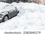 Small photo of City street driveway parking lot spot with small car covered snow stuck trapped after heavy blizzard snowfall winter day by big snowy pile. Snowdrifts and freezed vehicles. Extreme weather conditions