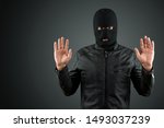 Small photo of Robber, a thug in a balaclava raised his hands on a black background, surrenders. Robbery, hacker, crime, theft, arrest. Copy space