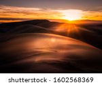 Sun setting over sand dunes in Colorado. The sky and sand is very orange. There are sun rays and a little lens flare.