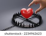 Small photo of Hand is trying to catch heart over a snare, a trap on a dark background. The concept of being trapped in love, being bound to love, coerced. Dangerous love.