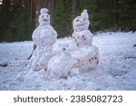 Small photo of Three snowmen in the forest against a background of coniferous trees, close-up. Family of snowmen.