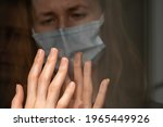 Small photo of Isolation of the coronavirus. Hapless dark-haired girl in a mask touches a woman's hand through a glass door during a house quarantine close-up. Social distance