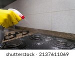 Close-up of a woman's hand in yellow gloves thrusting cleaning agent on the built-in kitchen stove
