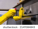 Women's hands in yellow rubber gloves are rubbing cleaning agent on the surface of the oven in the home kitchen. Concept of housework and housekeeping