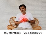 Small photo of Middle aged, senior Asian man with sudden onset of heart disease showing pain heart muscle leaks tired and suffocating sits on a wooden chair in agony : Myocardial infarction (Heart Attack)