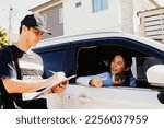 Small photo of Young woman smiling driving car and holding identity card to contact male security guard entering the housing estate for permission and recording information in order to comply with safety measures.