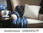 Small photo of Plain canvas throw pillow suitable for mock up mockup on a chair with blue throw blanket - your design, message or logo