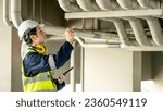 Small photo of Building inspector man using digital tablet pointing at plumbing pipeline system. Asian male worker in green vest, protective ear muffs and safety helmet working for building maintenance inspection