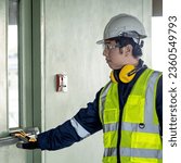 Small photo of Building inspector man pushing panic bar or crash bar on fire exit door. Asian male construction worker with reflective vest, safety helmet and goggles checking door hardware for safety and security