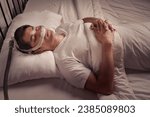 Small photo of Peaceful Asian male asleep using CPAP mask and machine for obstructive sleep apnea and snoring remedy