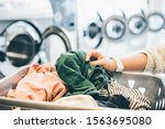 interior of small laundromat in daylight. Close-up female holding basket. Girl loading=