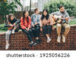 Multiracial young people playing guitar and singing on street.