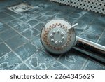 Silver shower head with limescales that should be cleaned and mold on tiles. Calcified shower due to hard water. Calcium mineral buildup.