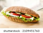 A sandwich with tomato, cucumber, feta cheese, lettuce on wooden board