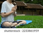 Small photo of Close up with Young Asian male pay obeisance or raise hand and doing meditation on yoga mat in the lawn.