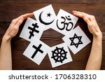 World religions concept. Hands hugs Christianity, Catholicism, Buddhism, Judaism, Islam symbols on wooden background top view