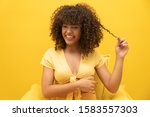 Happy laughing American African woman with her curly hair on yellow background. Laughing curly woman in sweater touching her hair and looking at the camera.