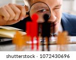Man in suit look thru loupe on statuettes closeup in office. Success hr assessment people headhunt inspector applicant exchange concept