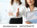 Small photo of Focus on tender female hands reaching precious arm to shake hands with somebody. Joyful woman holding important paper tablet with charts and graphs. Accounting office concept. Blurred background