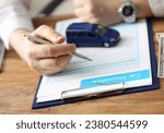 Small photo of Close-up of businessman signing car insurance document on table. Blue auto model standing on paper. Collision damage waiver. Transport business and protection concept