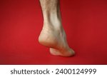 Small photo of Close-up of heel of foot with bad skin covered with cracks. Female gam exposed to camera on lower view angle. Moisturizing cream advertisement concept. Isolated on red background