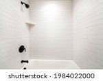 Small photo of Alcove bathtub with black plumbing fixtures and white subway tiles wall surround. Inside a tub with wall mounted shower and faucet, and a single corner shelf on the wall.