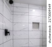 Small photo of Square Shower stall with mosaic tiles flooring and marble tiles surround with black grout. There is a a shower curtain on the left and wall-mounted black shower head fixtures on the right.