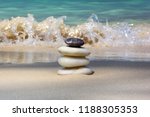 Small photo of Balanced pyramid of Zen stones on the beach. In the background a surge of wave. The concept of unwavering stability and balance.