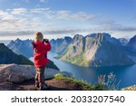 Cute child, standing on top of the mountains and looking down on Reine after climbing Reinebringen treeking path with lots of stairs, using binoculars to look at the view