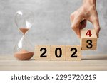hand flipping block 2023 to 2024 text with hourglass on table. Resolution, time, plan, goal, motivation, reboot, countdown  and New Year holiday concepts