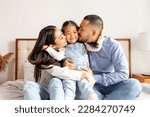 Small photo of happy young asian family sit on bed together with daughter, korean little girl hug and love parents at home, mom and dad kiss daughter