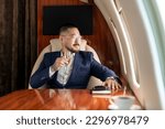 successful Asian businessman in suit and glasses sits in private jet and drinks champagne, Korean manager in business clothes flies in business class and looks out the window, luxury lifestyle