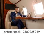 asian businessman in suit and glasses with glass of champagne flies in luxury jet and uses smartphone, korean entrepreneur films himself on the phone and communicates via video call