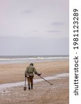 Small photo of Bergen aan Zee, The Netherlands - April 30, 2021: Professional beachcomber with metal detector searching the beach for residual and valuable materials on overcast day at Dutch seaside shore