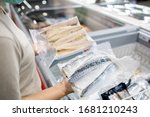 Asian woman wear face mask,choosing packed frozen cut fish in freezer in food department of supermarket,people panic buying, hoarding during the Covid-19,Coronavirus spread,girl preparing for pandemic