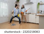 Small photo of Joyful woman singing songs and dancing with closed eyes while cleaning kitchen at home. Happy young couple having fun while doing cleaning the floor at home and pretend to sing song with mop.