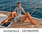 Couple in love sitting on yacht deck while sailing in the sea. Handsome man and beautiful woman having romantic date. Luxury travel concept.