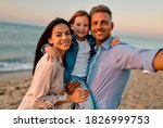 Happy family concept. Young attractive mother, handsome father and their little cute daughter standing together on the beach and making selfie.