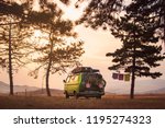 Old timer camper van parked on the top of the hill between pine trees in the beautiful sunset sky