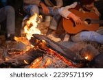 Small photo of Unrecognizable friends having fun playing music and enjoying bonfire camping in nature at night. Group of people chilling at fire in the evening, camping in the forest near lake. High quality photo