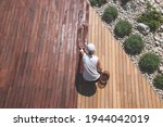 Small photo of Wood deck renovation treatment, the person applying protective wood stain with a brush, overhead view of ipe hardwood decking restoration process