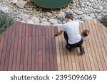 Hardwood deck oil application, overhead woman painting wood boards of garden decking